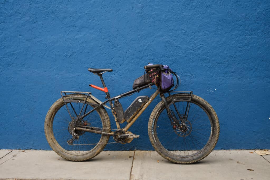 Dirty bikepacking mountain bike with Old Man Mountain Racks, in front of a blue background